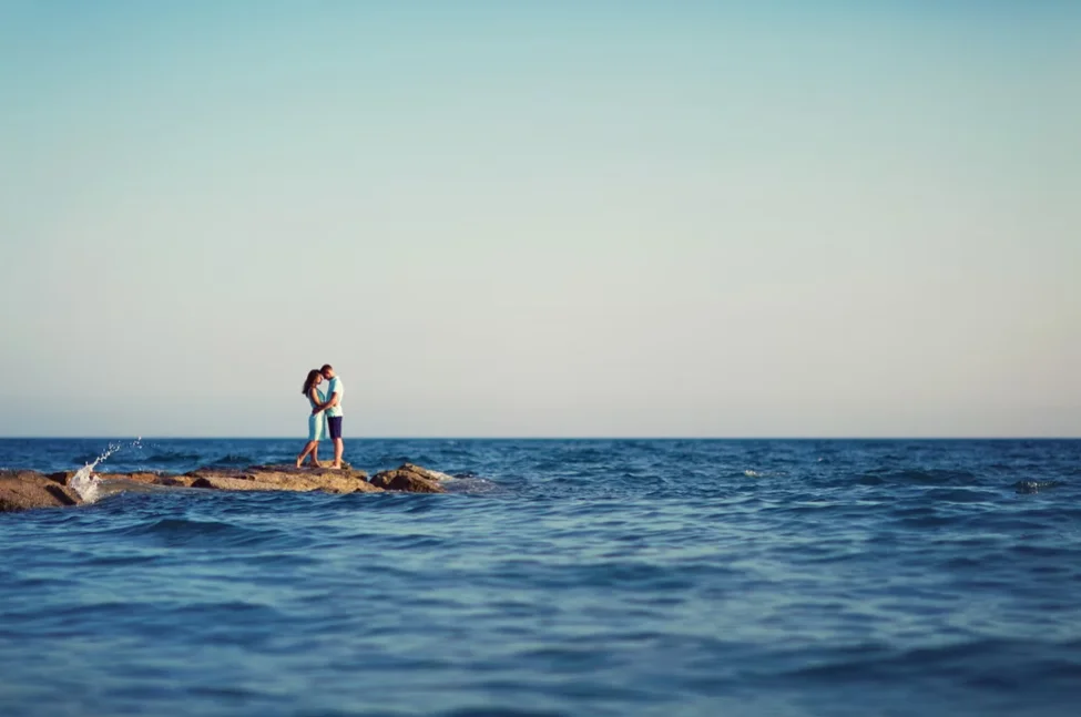 Bride and groom embrace on the rocks overlooking the sea