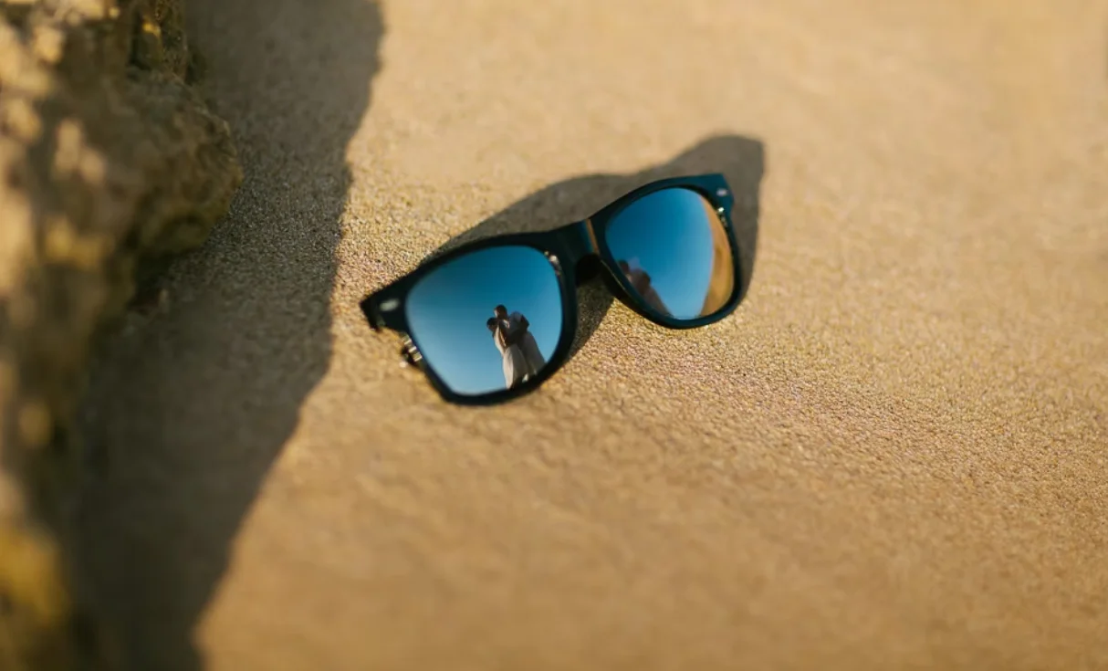 Sunglasses in sand reflecting a couple embracing