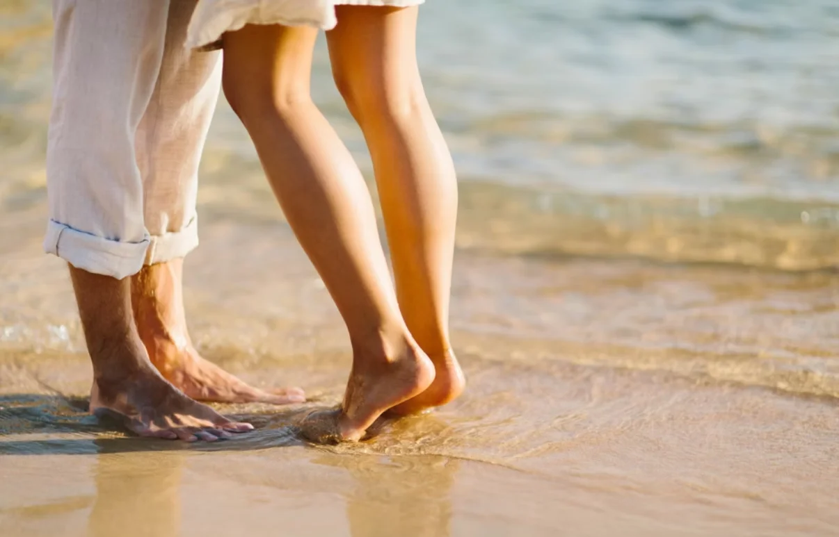 Man and woman's feet at the shortline with the tide coming in over them