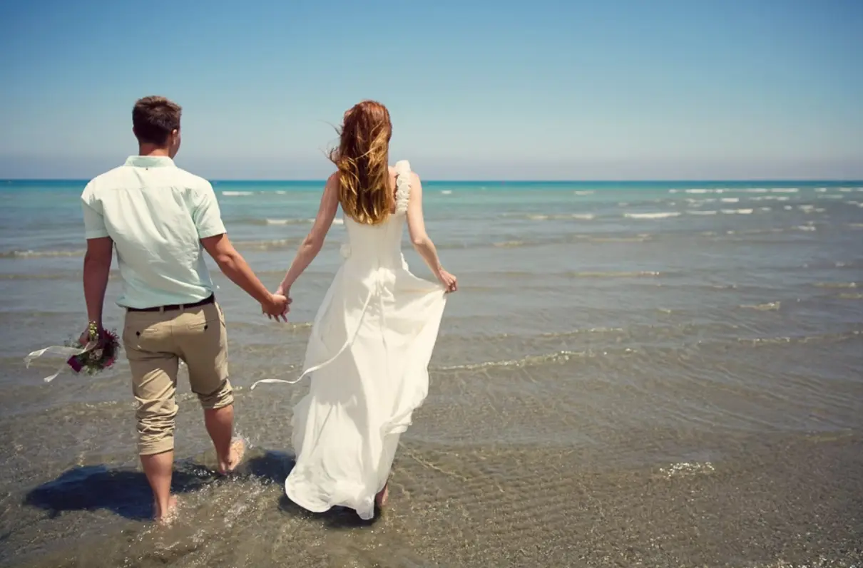Barefoot couple holding hands while walking into the sea