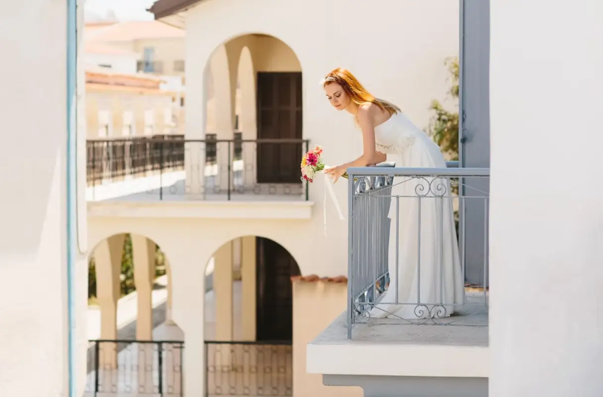 Bride leaning over the balcony looking below, holding a bouquet of flowers