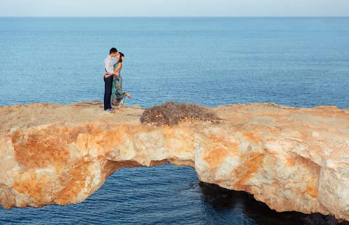 Couple embracing on a rock arch over the sea