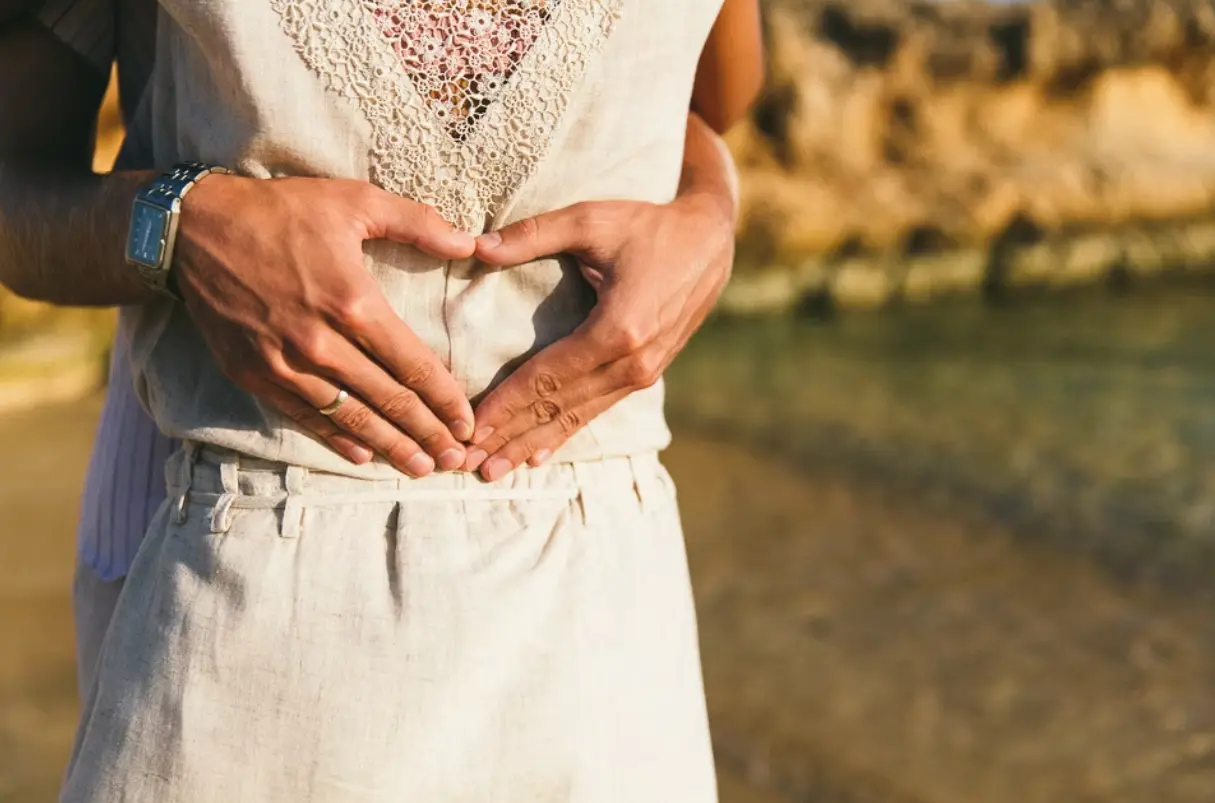 Love heart shape made with hands on womans back with the sea in the background