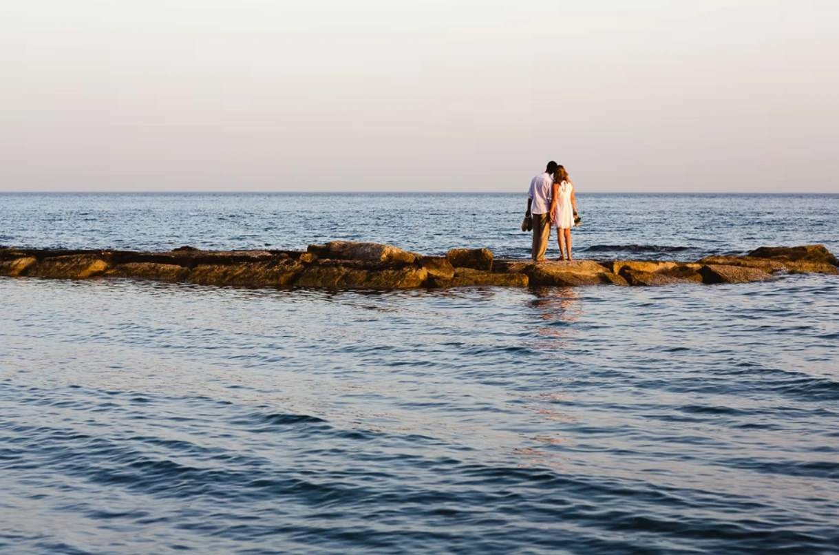 Bride and groom stood on rocks, looking out to sea