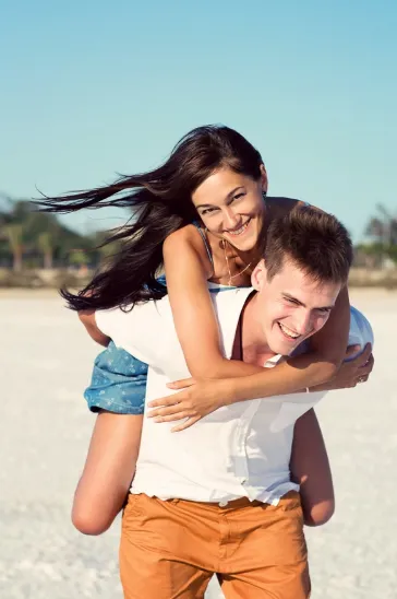 Couple lauging during playful beach photoshoot where one partner is giving the other a piggback