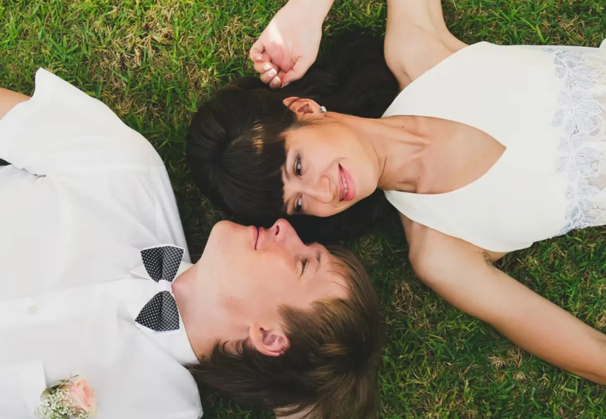Bride and groom lying on the grass and smiling at each other