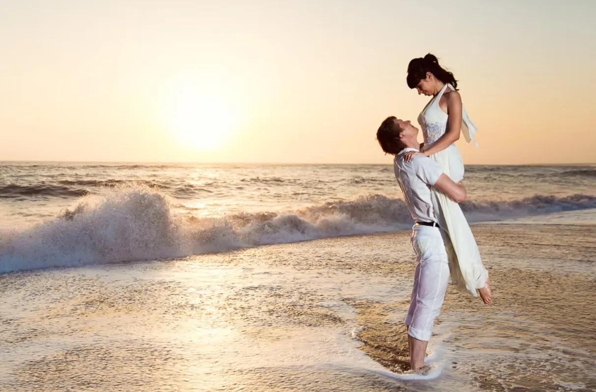 Playful couple with the groom lifting the bride in the air on the beach