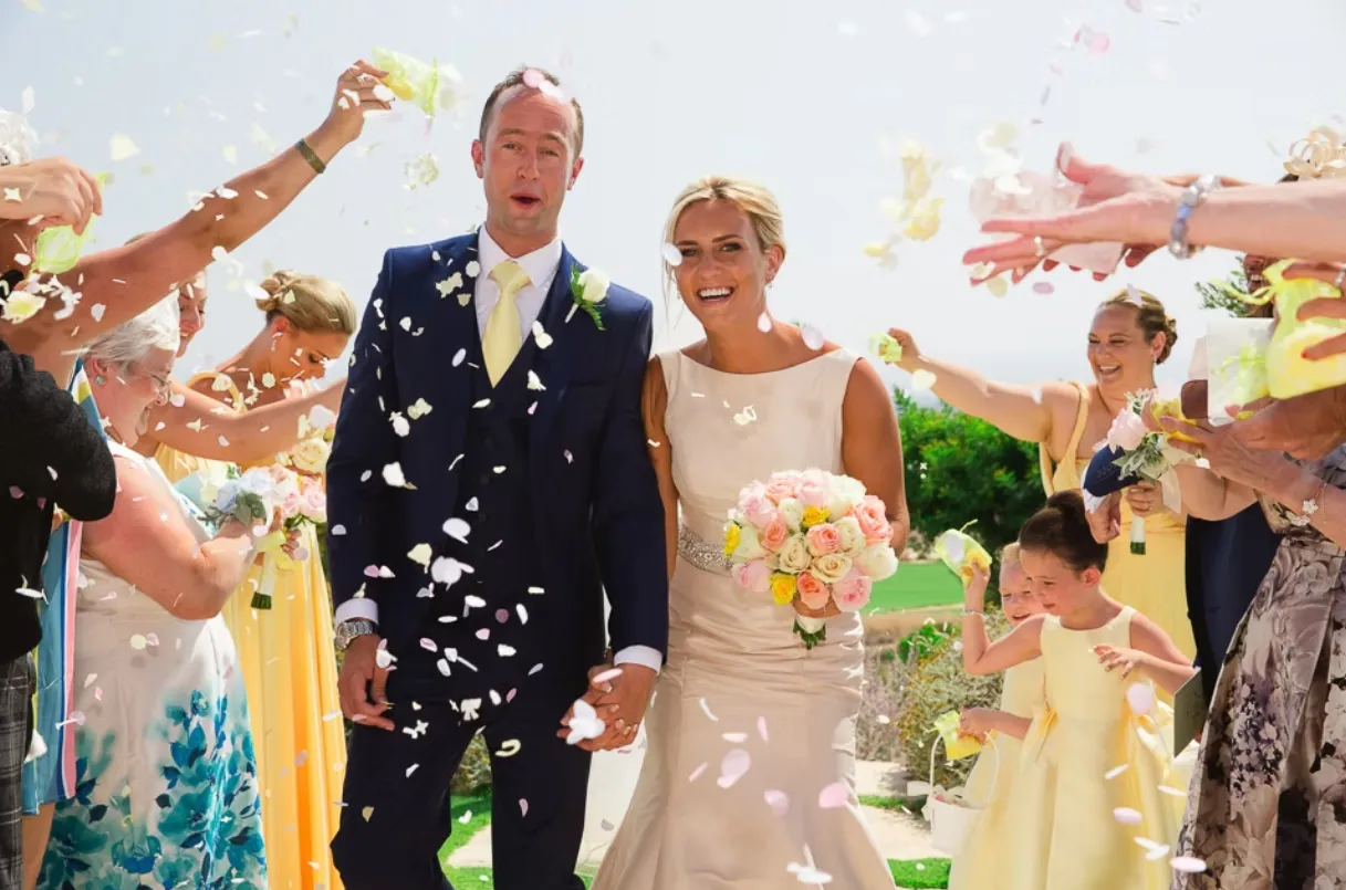 Newlywed coiple having confetti thrown at them as they walk down the aisle