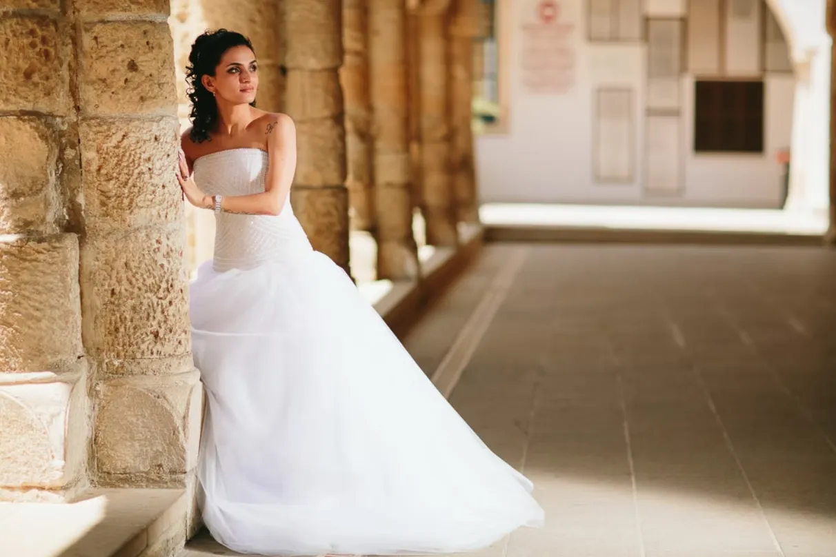 Bride in white wedding dress leaning against stone column during quiet portrait moment