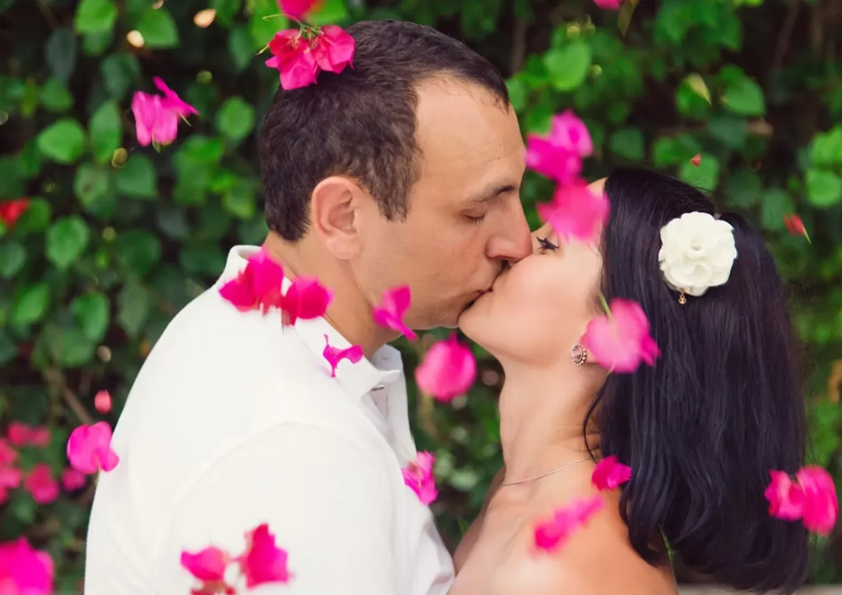 Couple kiss with rose petals falling around them during wedding photoshoot